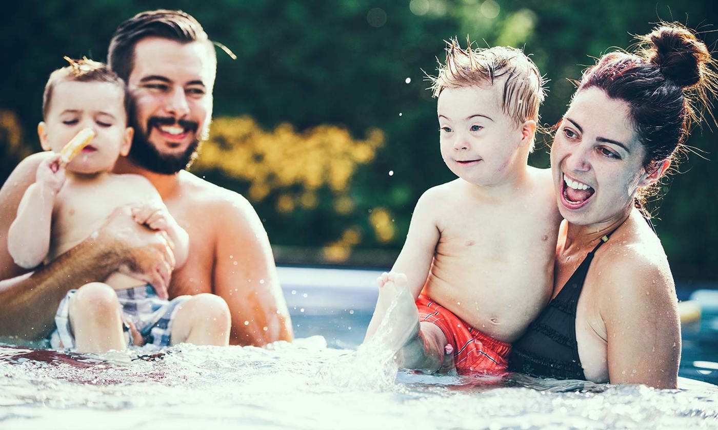 Little boy with Down syndrome eating popsicle in the swimming pool with his family