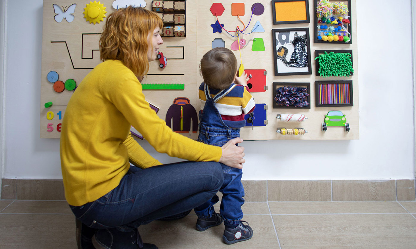 Mother and her one year old baby son playing with wooden interactive board.
