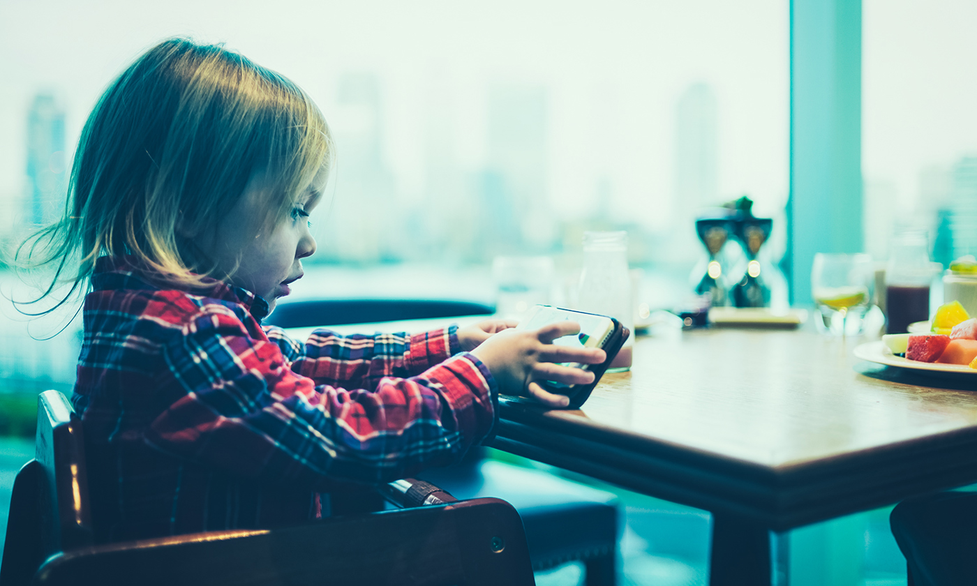 A toddler is using a smartphone at the breakfast table